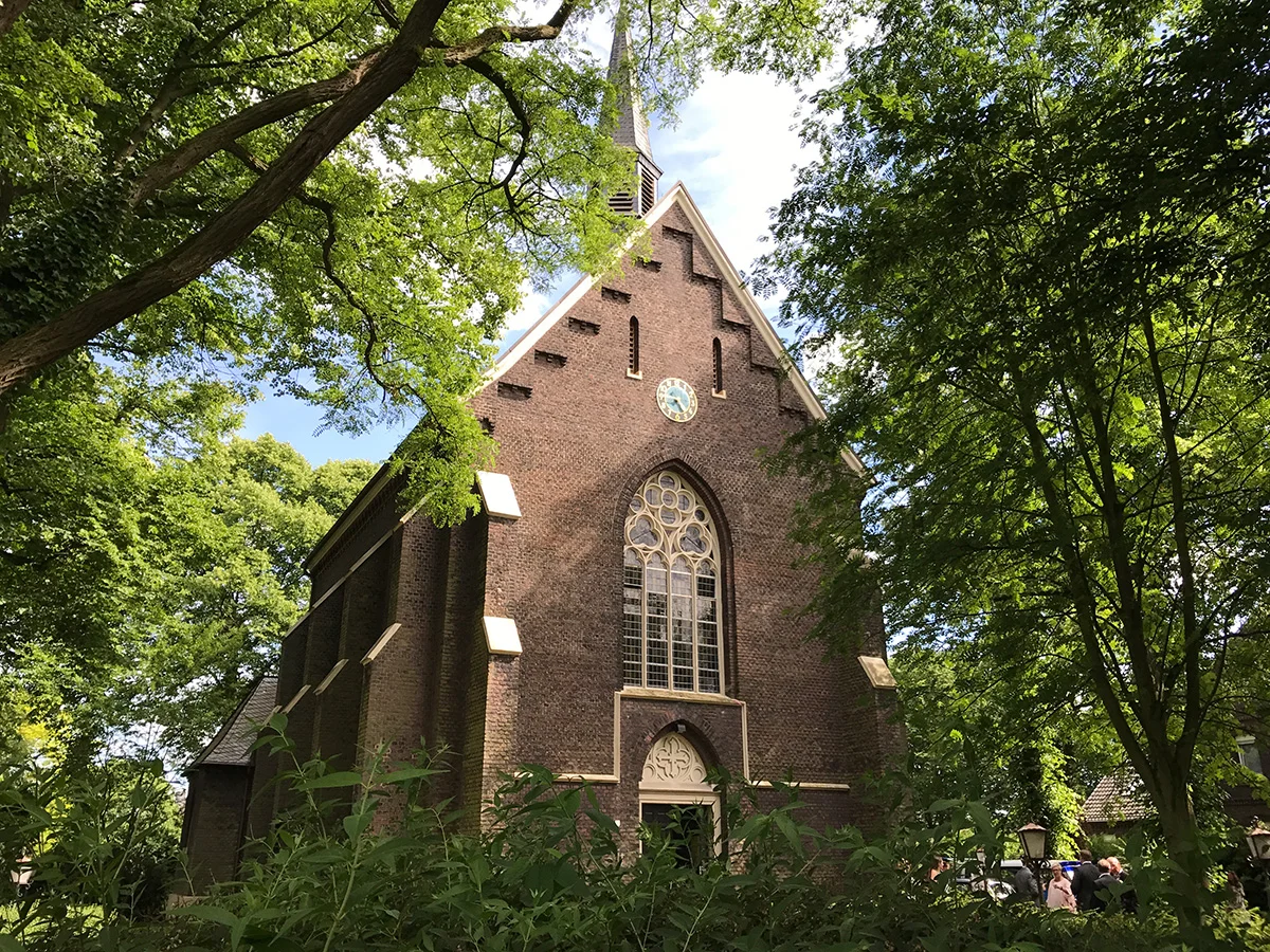 Außenansicht einer historischen Backsteinkirche umgeben von grünen Bäumen für eine kirchliche Trauung in NRW.